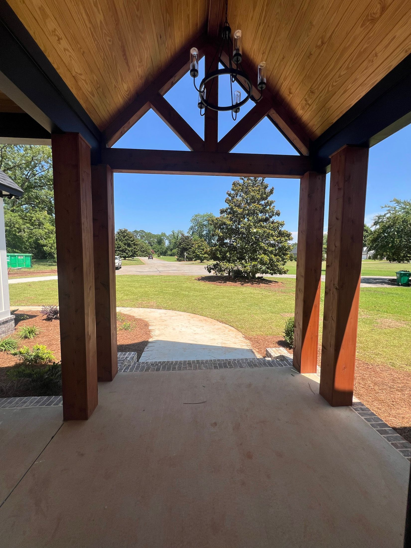 Covered entryway with wooden beams, view of a grassy lawn and tree.