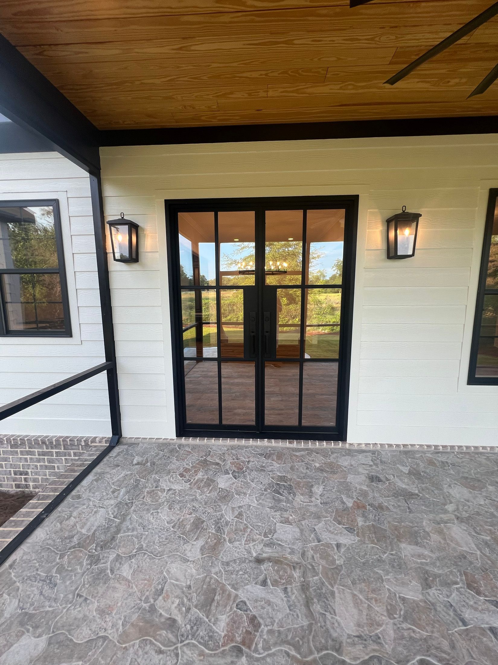 Black framed double doors on a porch with sconce lighting. Exterior view.