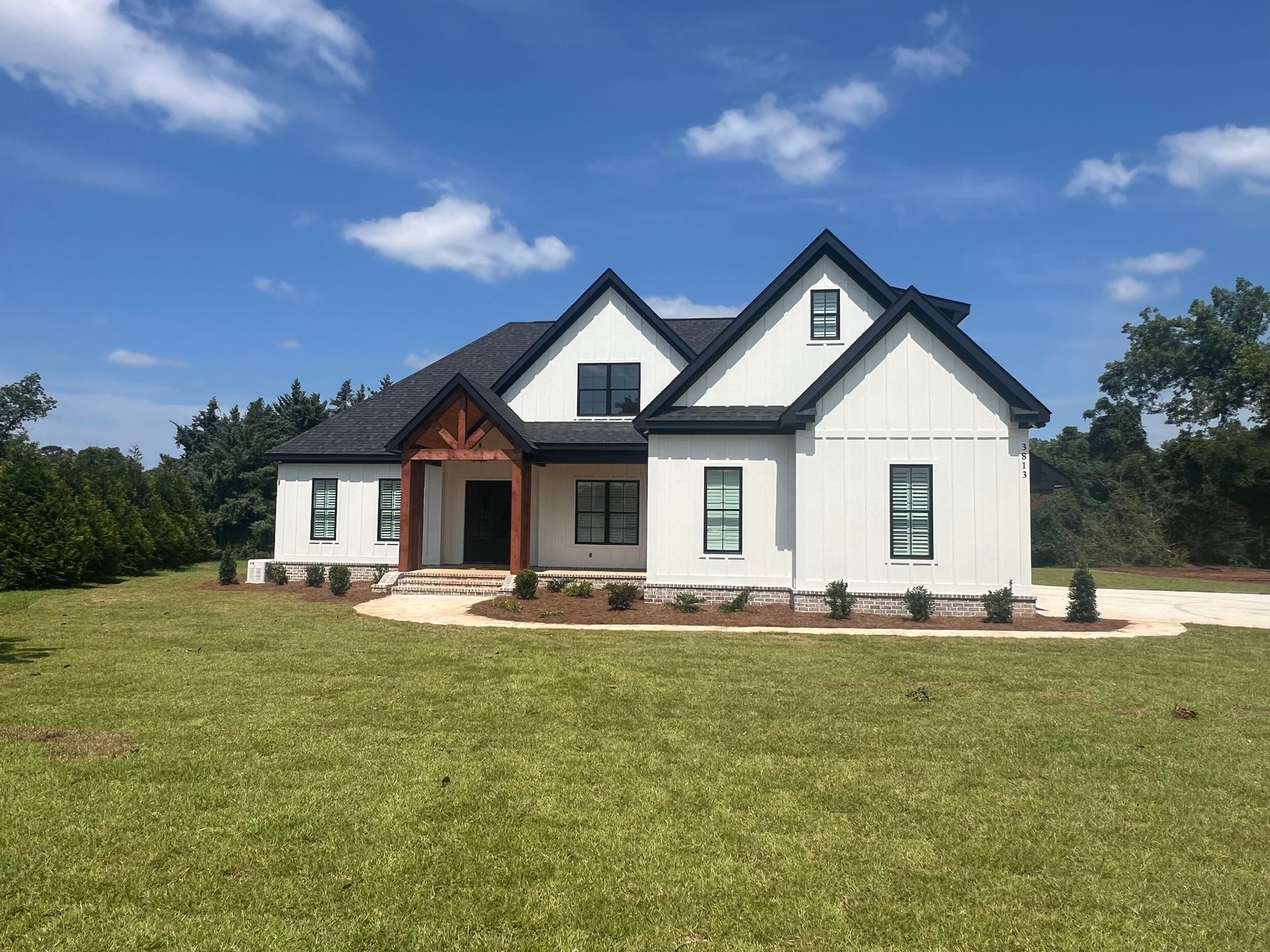 White farmhouse with black trim, a wooden porch, and a green lawn under a blue sky.