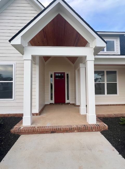 Beige house with white porch pillars and red door. Brown brick trim.