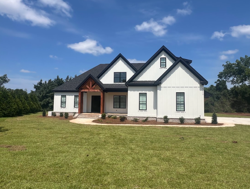 White farmhouse with black trim, and a porch, on a grassy lawn with a blue sky.