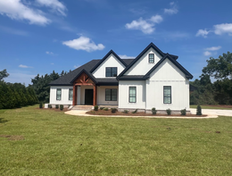 White farmhouse with black trim, surrounded by green grass and a blue sky.