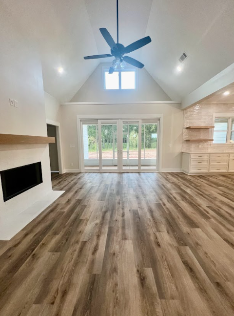 Interior of a modern living room with wood floors, fireplace, and sliding glass doors.  A black ceiling fan hangs overhead.