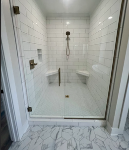 Glass-enclosed shower with white subway tile walls, built-in corner seats, and bronze fixtures. Hexagon tile floor.