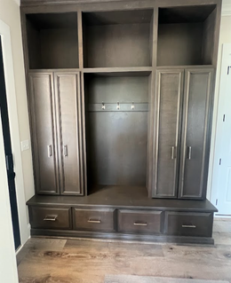 Built-in wooden entryway storage with cabinets, drawers, open shelf, and coat hooks. Gray-brown finish.