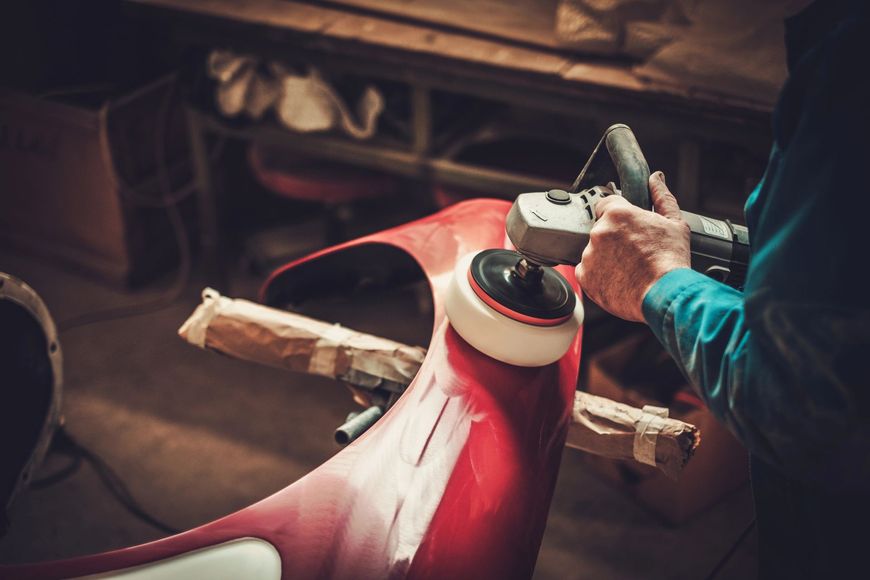 Persona che utilizza un elettroutensile per lucidare un pezzo rosso di un'auto in un'officina.