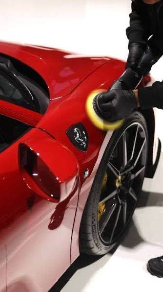 Una persona con guanti neri lucida il cofano di un'auto blu con una lucidatrice in un garage.