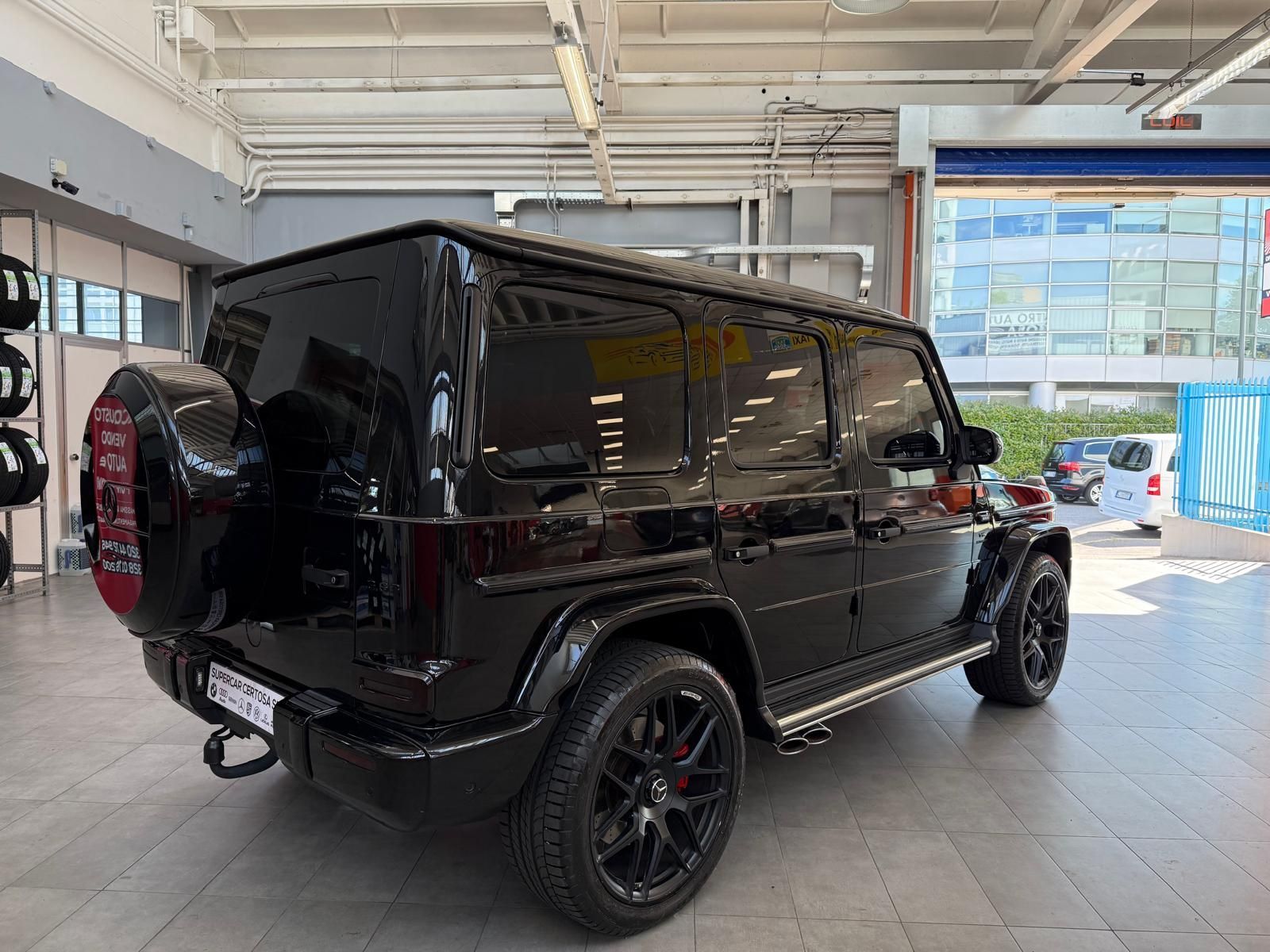 Un SUV Mercedes-Benz Classe G nero parcheggiato in un garage. Ha cerchi neri, ruota di scorta e vetri oscurati.