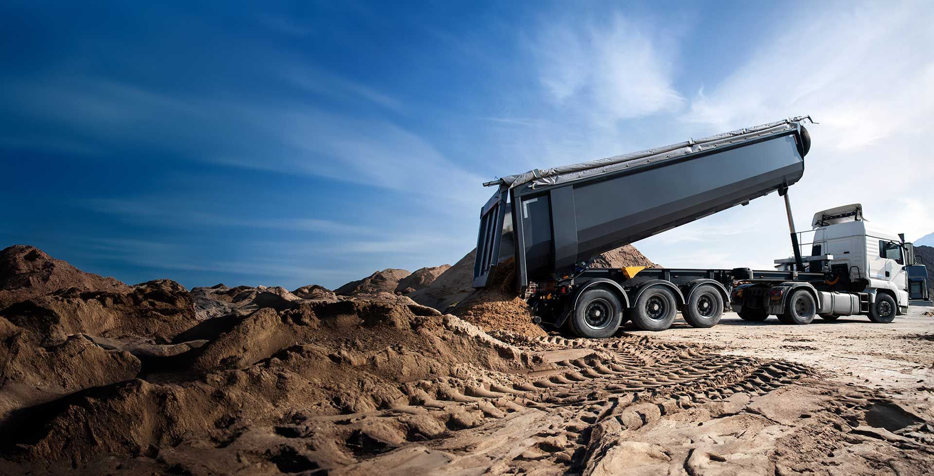 A dump truck is in the process of dumping sand onto a dirt road 

