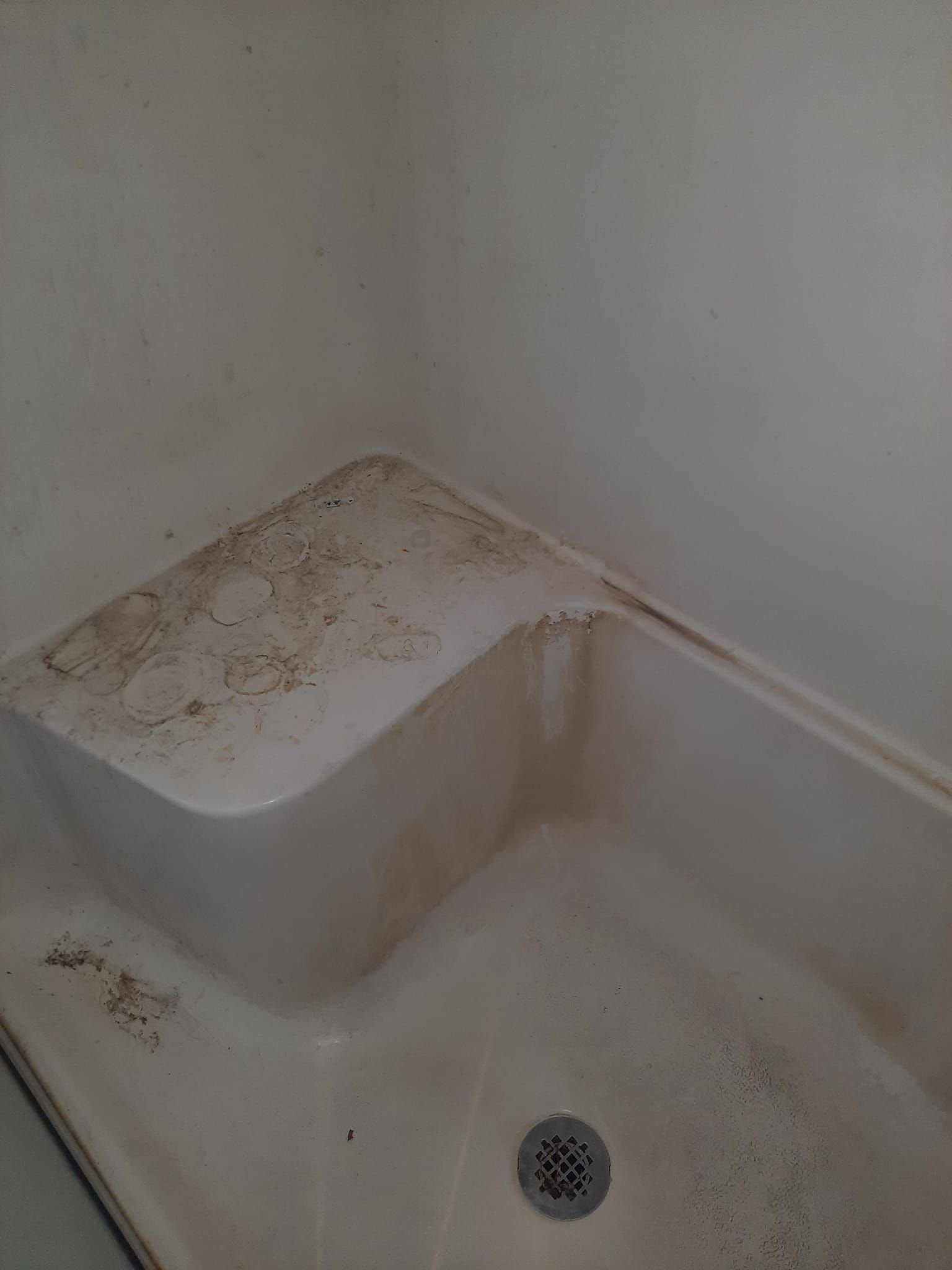 A dirty bathtub with a drain in a bathroom.