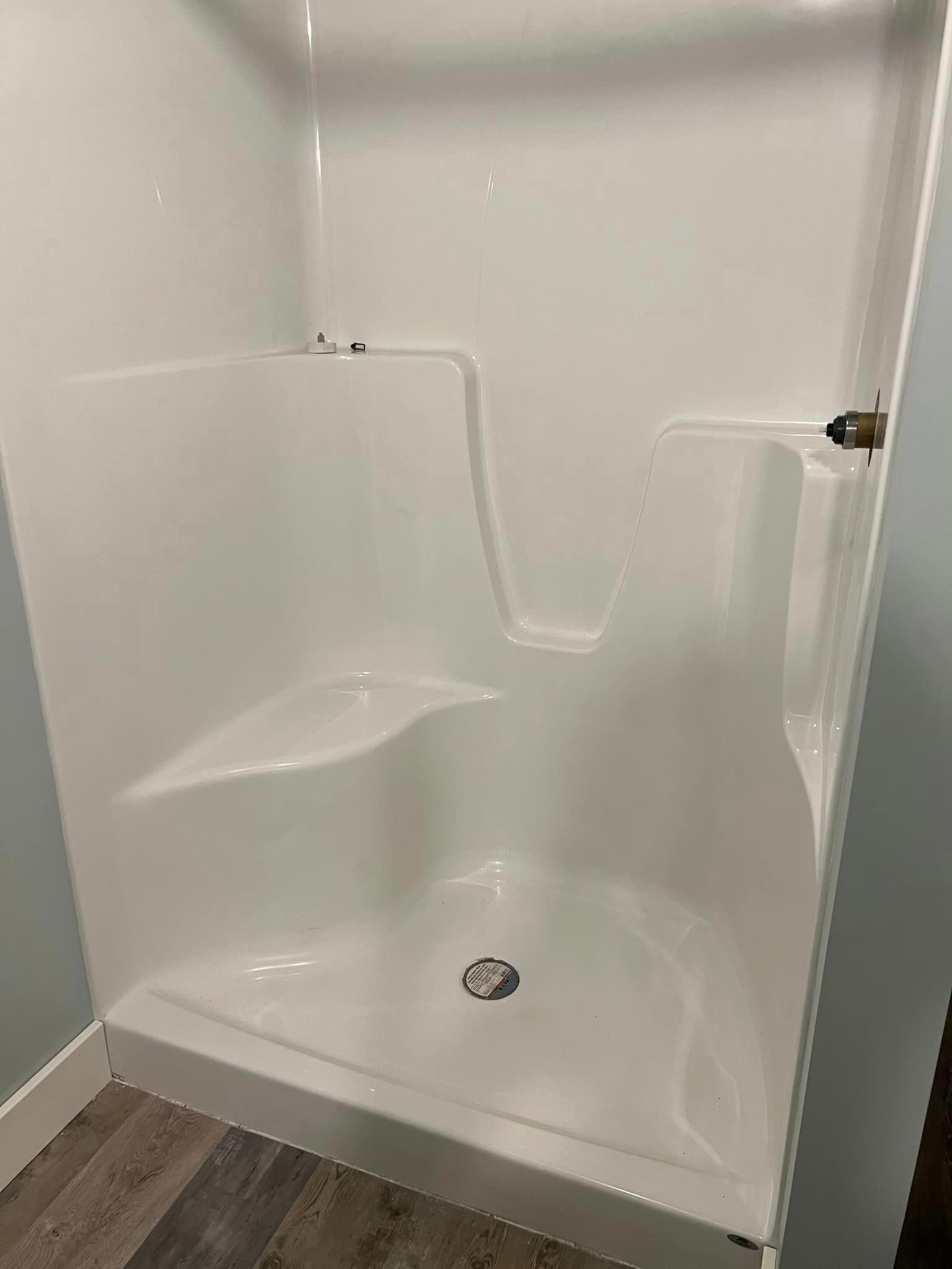 A white shower stall with a seat and a drain in a bathroom.