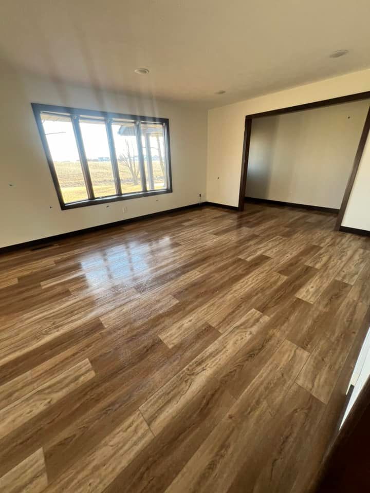 An empty living room with hardwood floors and a large window.