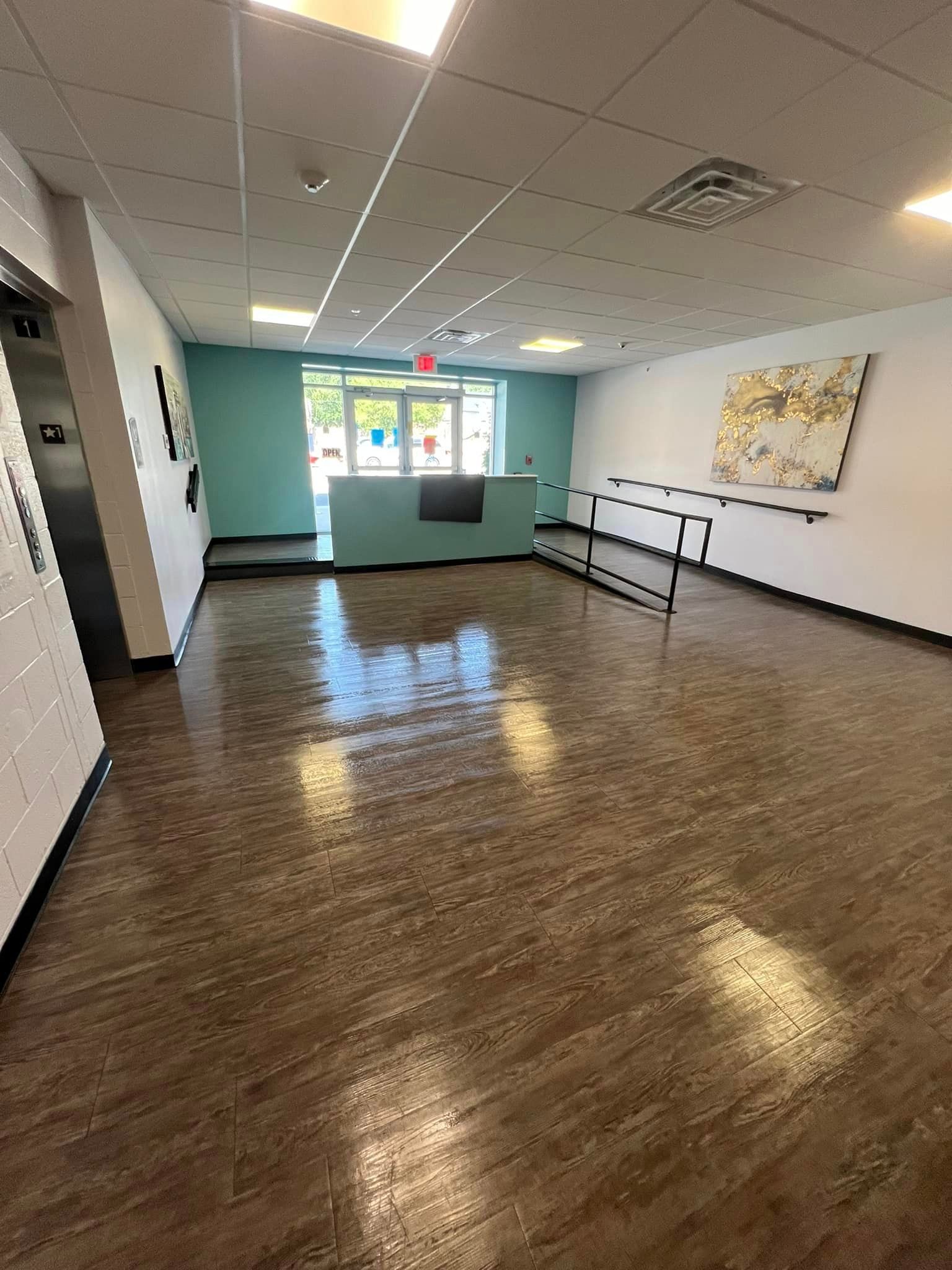 A large empty room with a wooden floor and a painting on the wall.