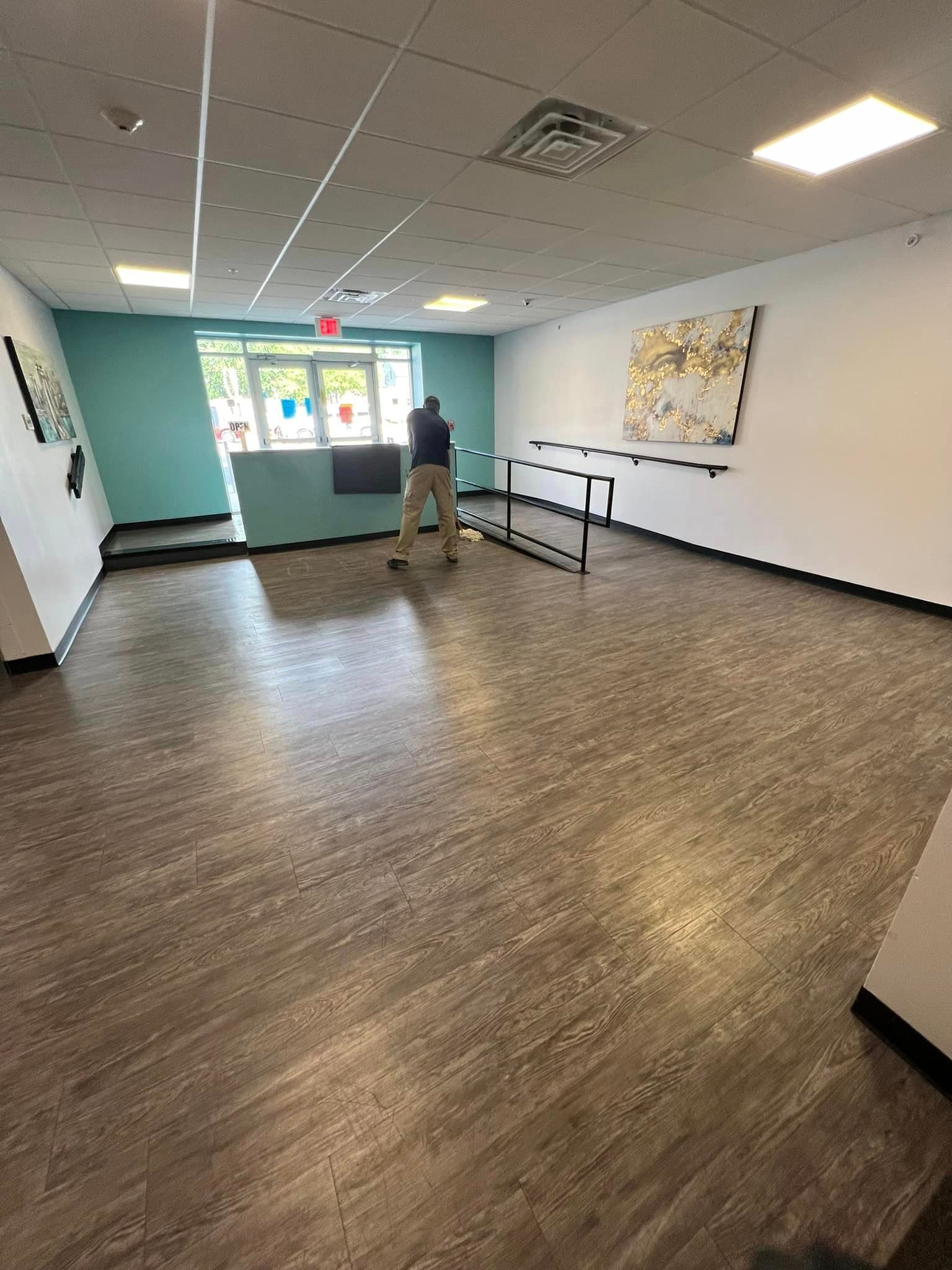 A man is standing in a large room with a wooden floor.