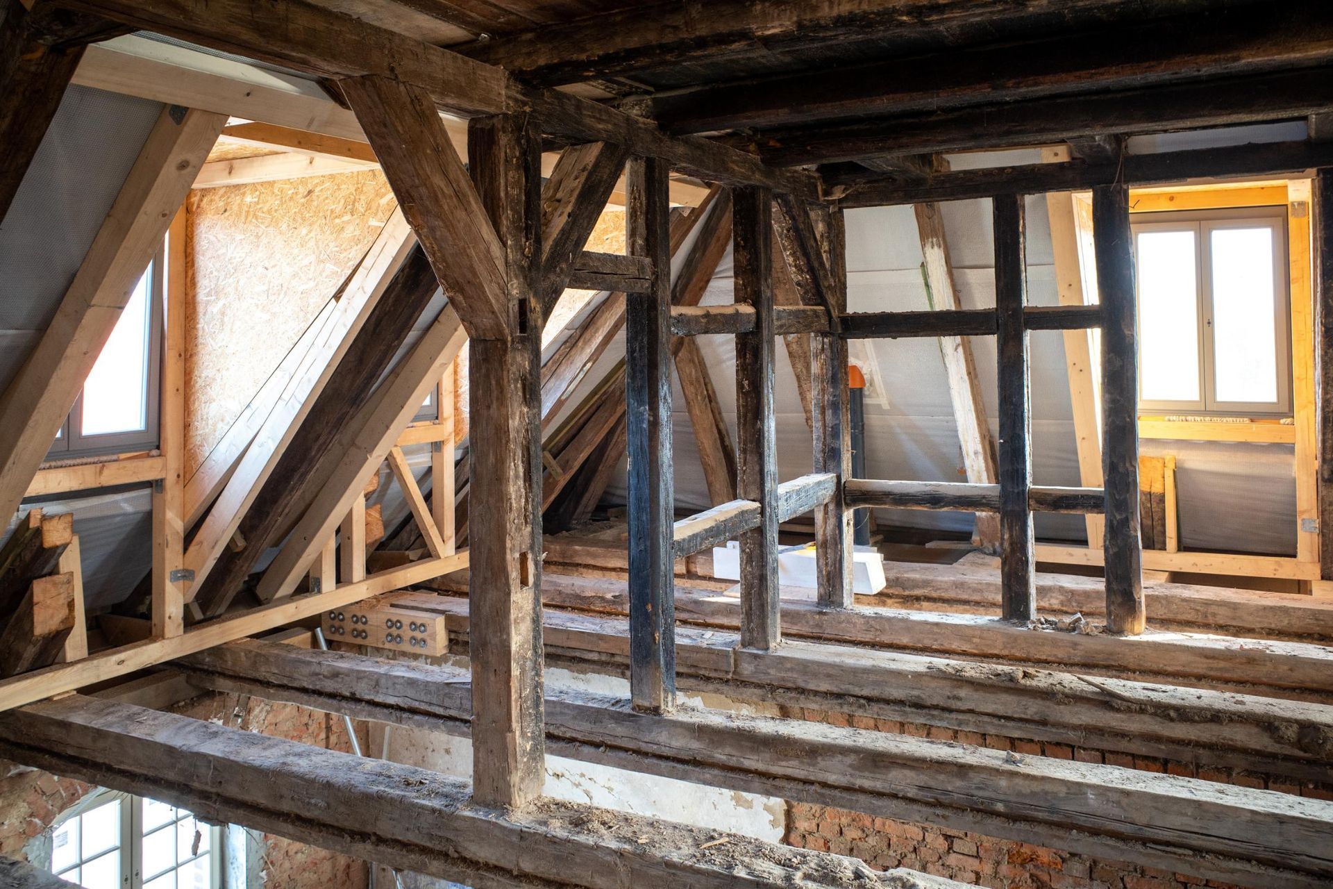 Interior view of a wooden attic frame during renovation, showing exposed beams, natural light, and structural details.
