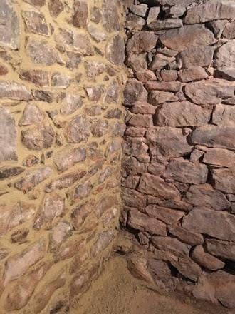 Stone walls meet at a corner. One wall is light with tan mortar, the other dark and rough.