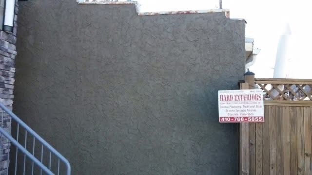 Gray stucco wall with a business sign, next to a wooden fence.