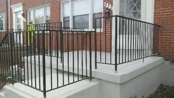 Black metal railing on a concrete porch leading to a brick house.