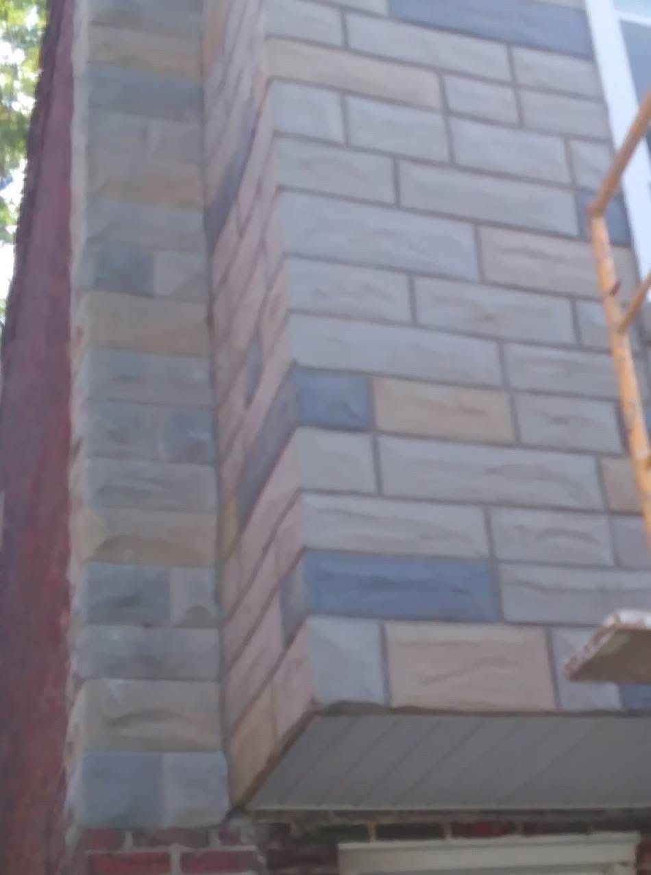 Corner of building with blue, tan, and gray stone facade, next to red brick wall.