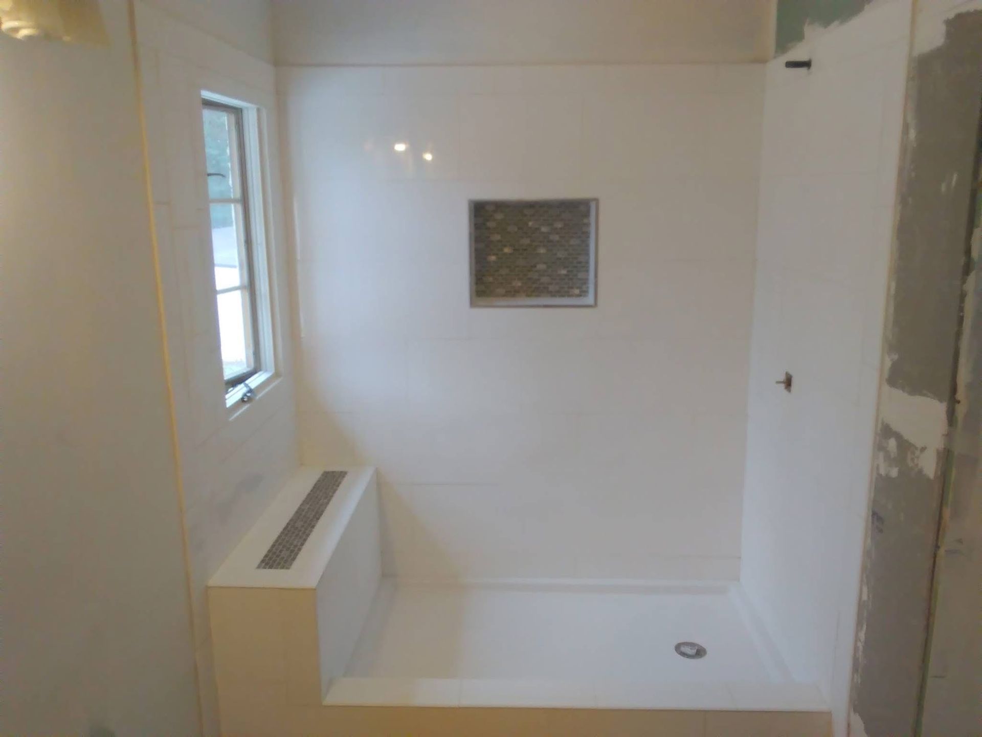 White shower stall with seat, small window, and decorative tile insert.
