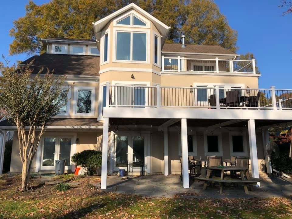 Beige multi-level house with white trim, multiple decks, and a view of trees. Sunny day.