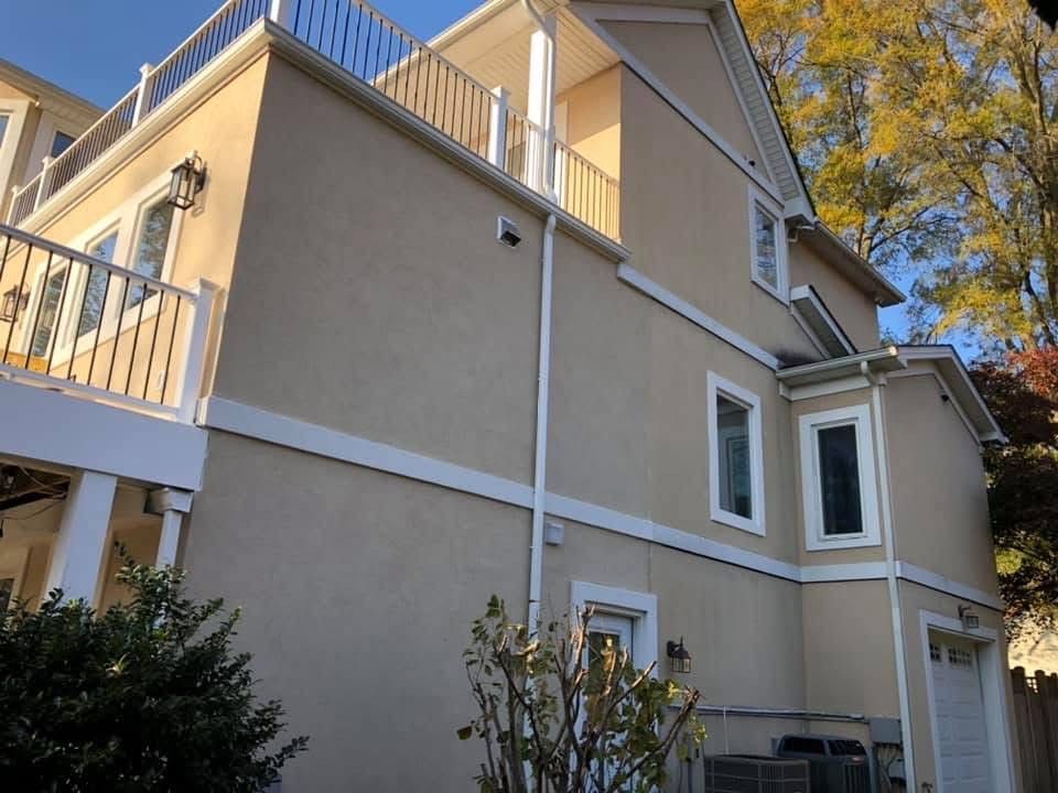 Beige stucco house with white trim, balcony, and trees against a blue sky.