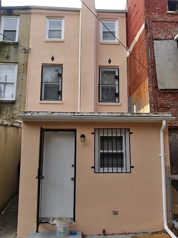 Rear exterior of a light peach building with windows, a door, and black security bars.