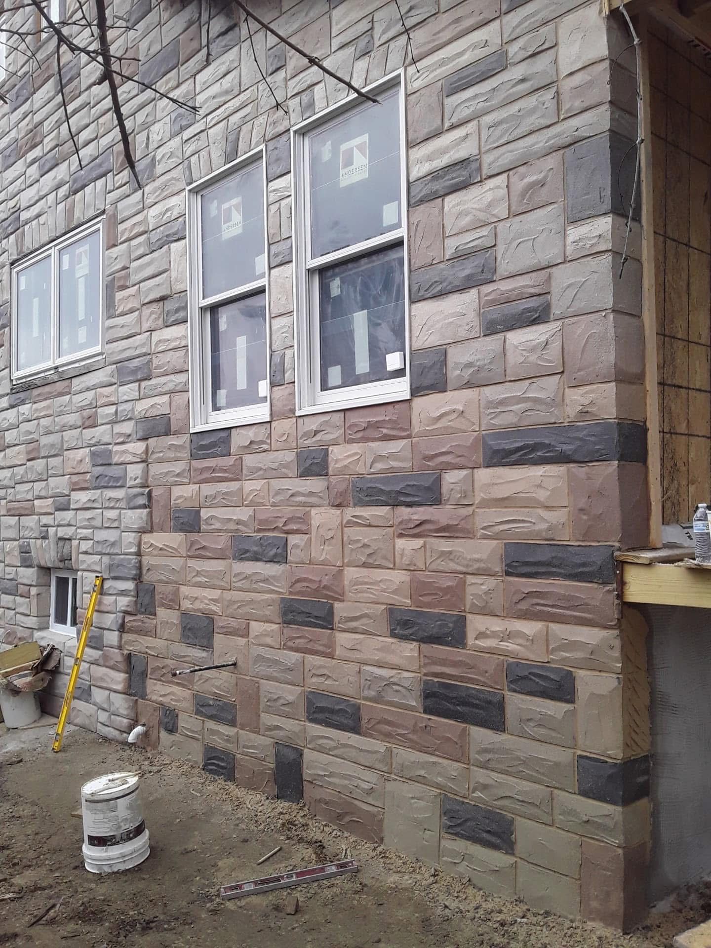 Exterior of a building with brick veneer siding in shades of brown, gray, and black. Windows are installed.