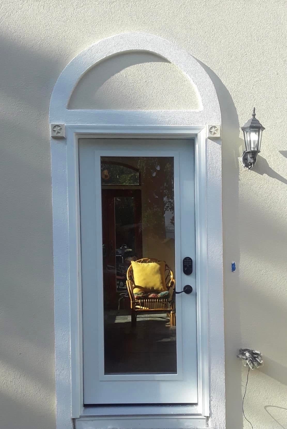White door with arched top on a stucco wall. A lamp and decorative trim are visible.