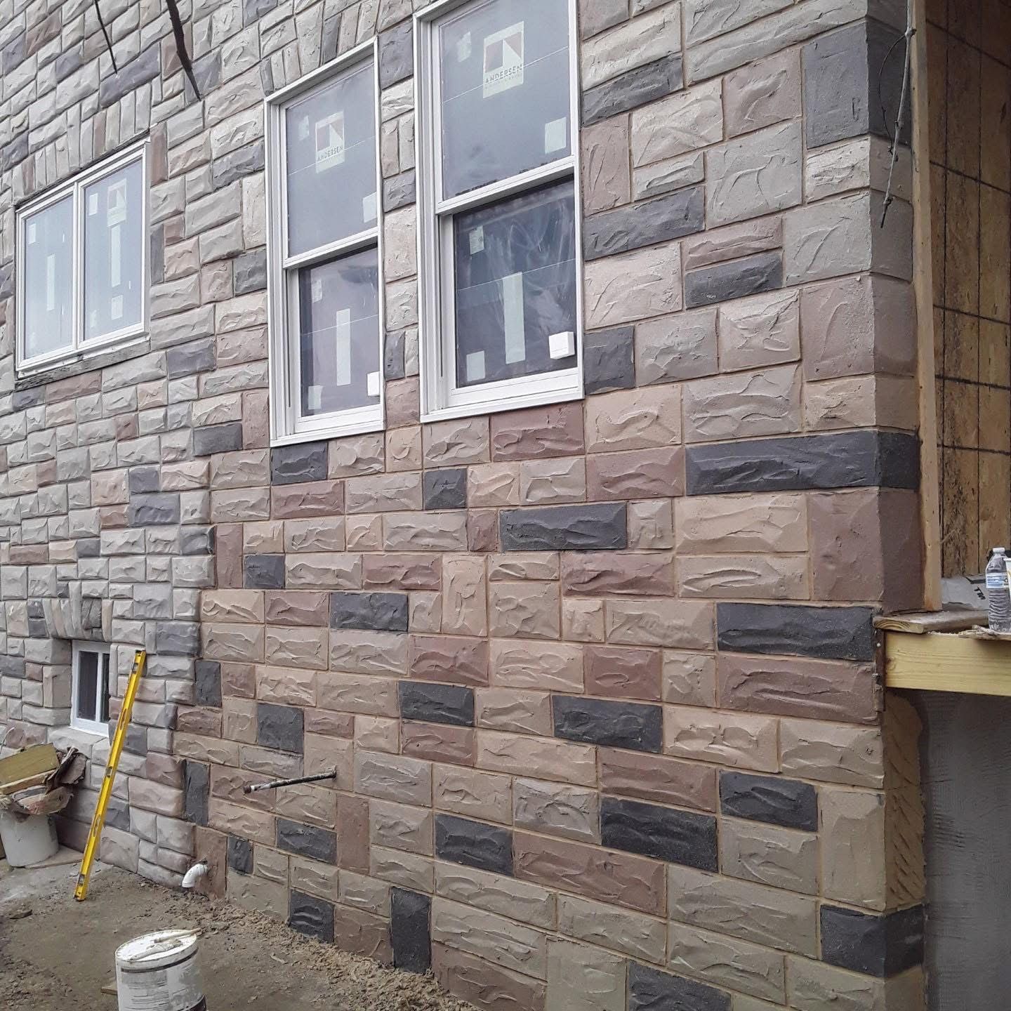 Exterior wall of a building with stone veneer in shades of brown, gray, and black. Windows are visible.