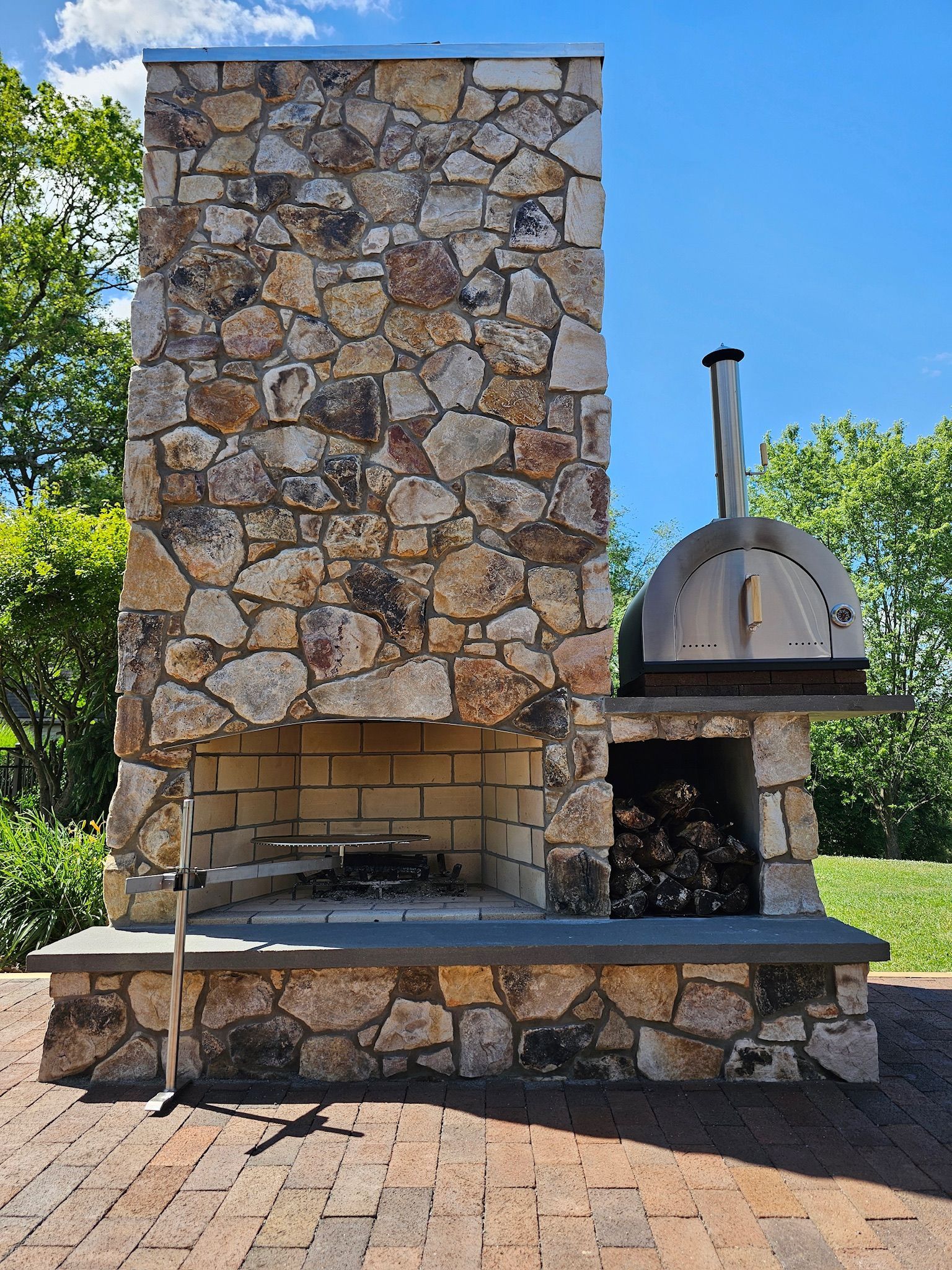 Outdoor stone fireplace with a pizza oven attached, and firewood in the storage.