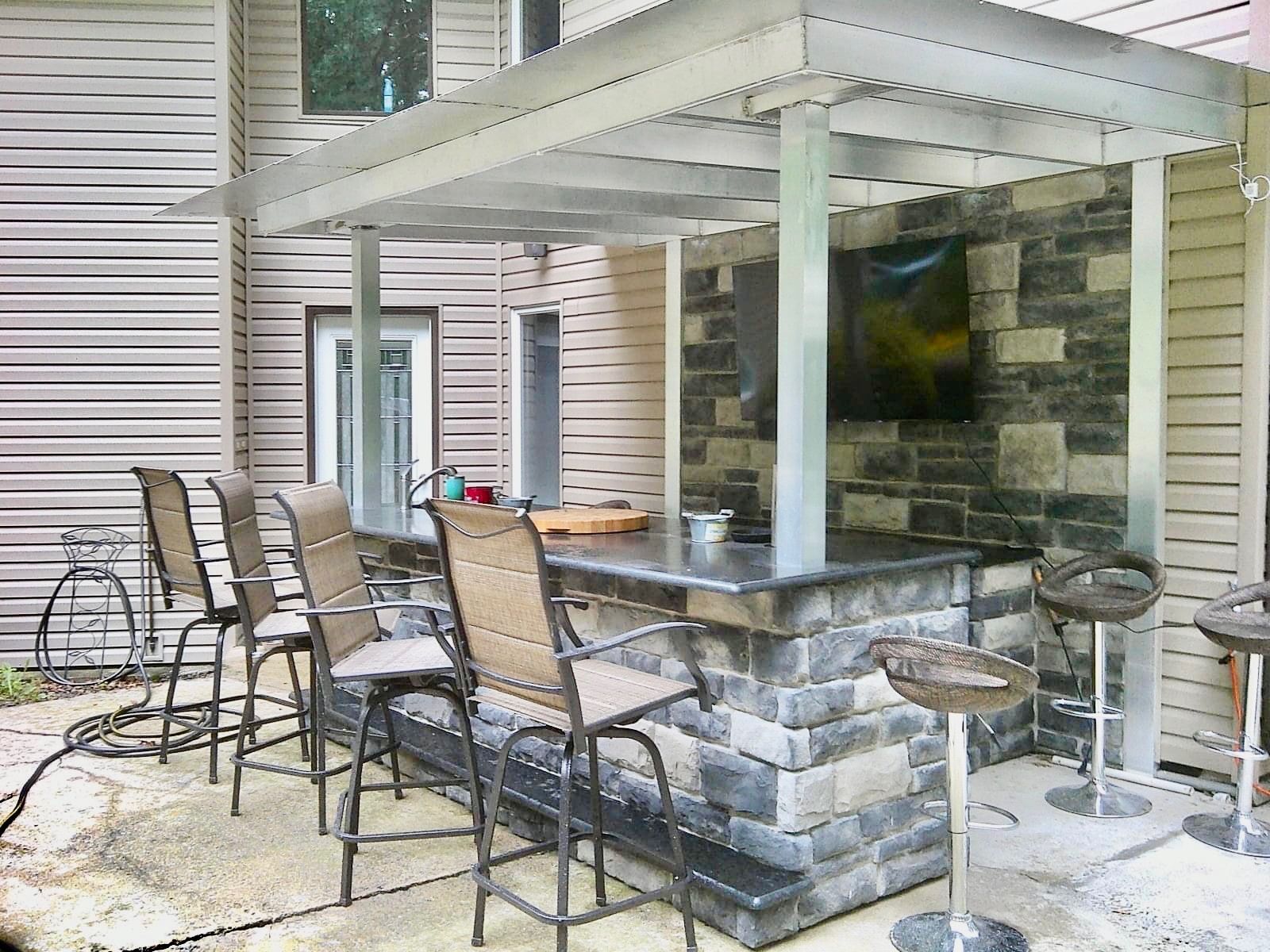Outdoor bar with stone base, metal frame, bar stools, and a TV.