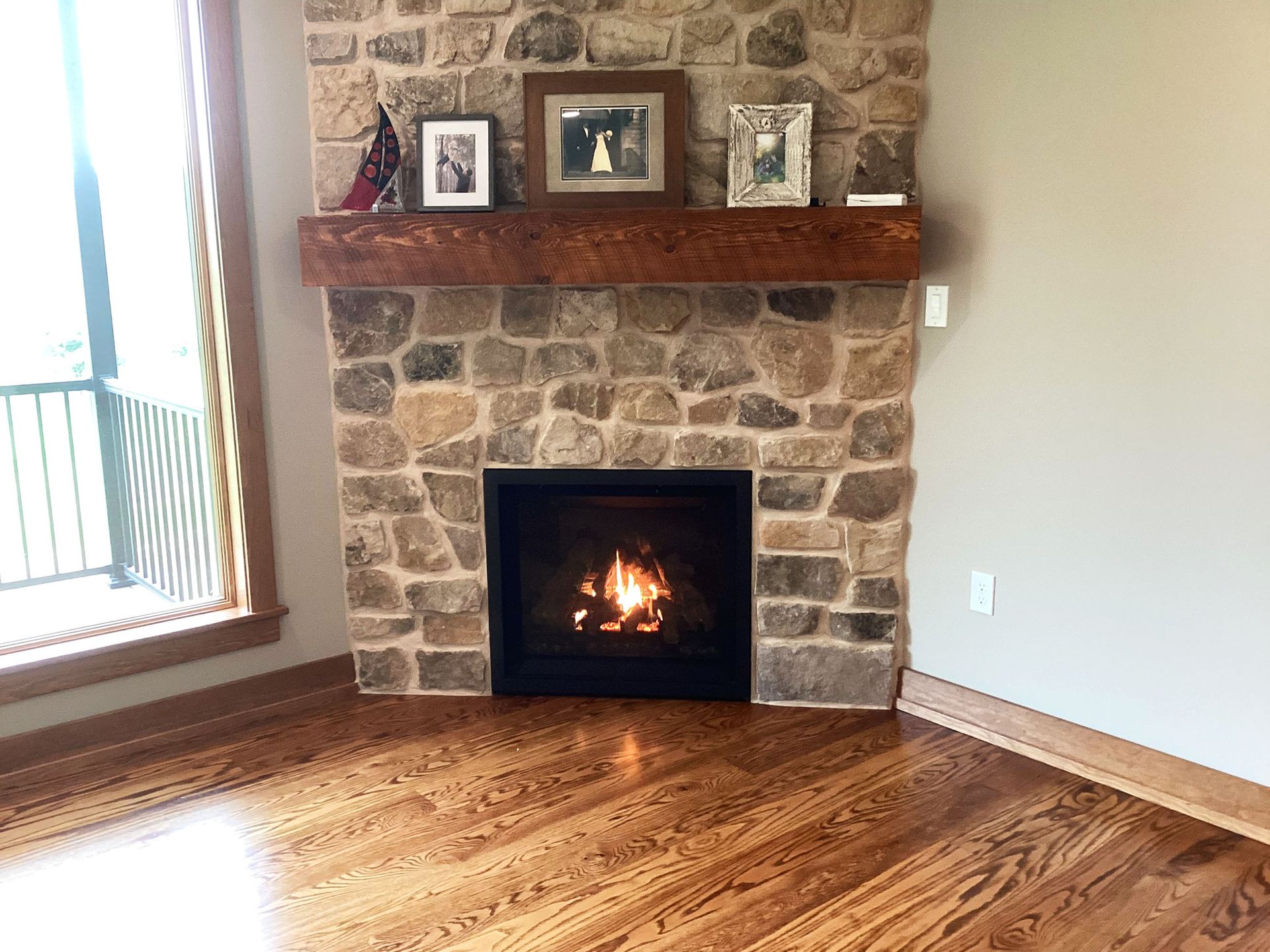 Fireplace with stone surround, wooden mantel, and three framed photos above, hardwood floor.