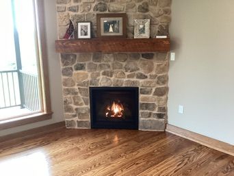 Fireplace with burning fire, stone surround, wooden mantel, photos, and hardwood floor.