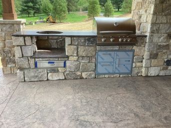 Outdoor kitchen built with stone, includes grill, storage, counter and pizza oven in a stone enclosure.