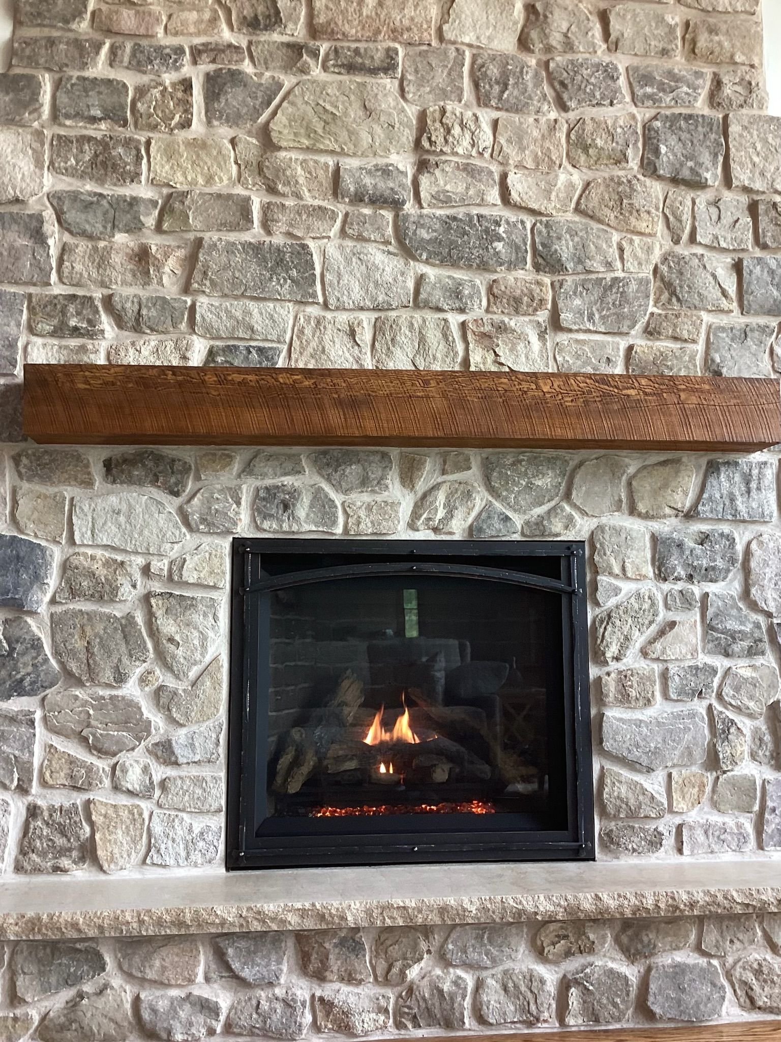 Fireplace with stone surround, lit fire, and wooden mantel.