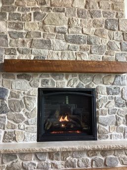 Fireplace with stone surround, lit fire, and wooden mantel.