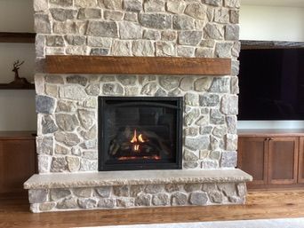 Fireplace with stone facade, dark metal firebox, wooden mantle, and stone hearth.