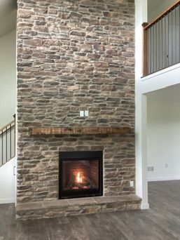 Stone fireplace with lit fire, wooden mantle, and a staircase in the background.