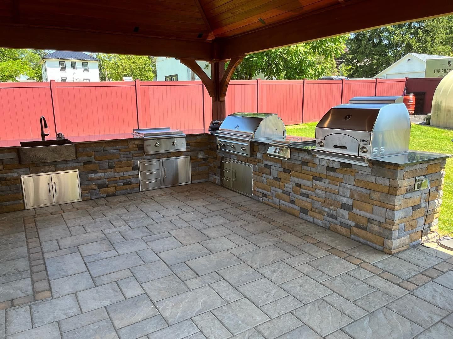 Outdoor kitchen with grills, stone facade, and red fence.