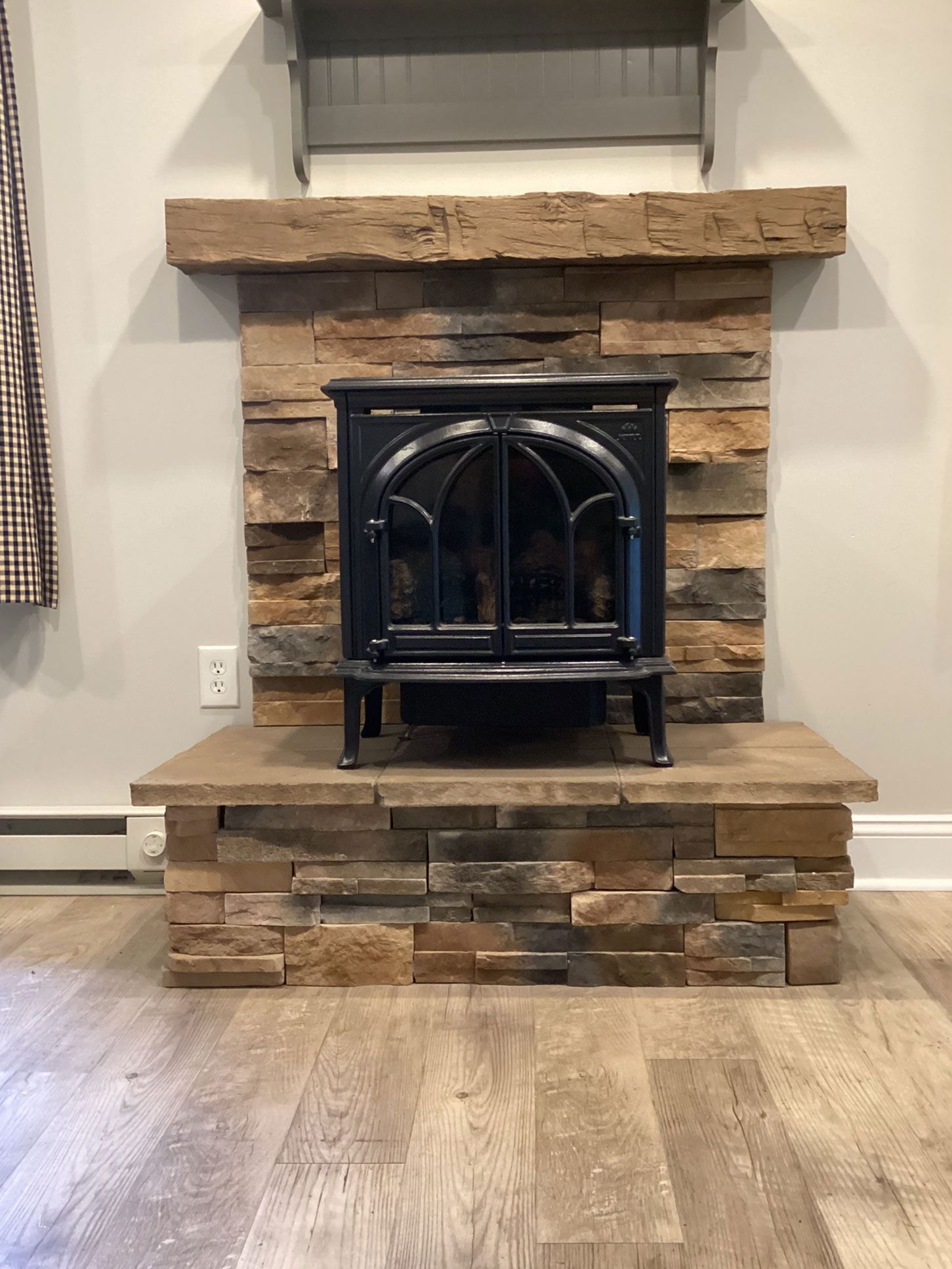 Electric fireplace in a stacked stone surround, with a wood mantle.
