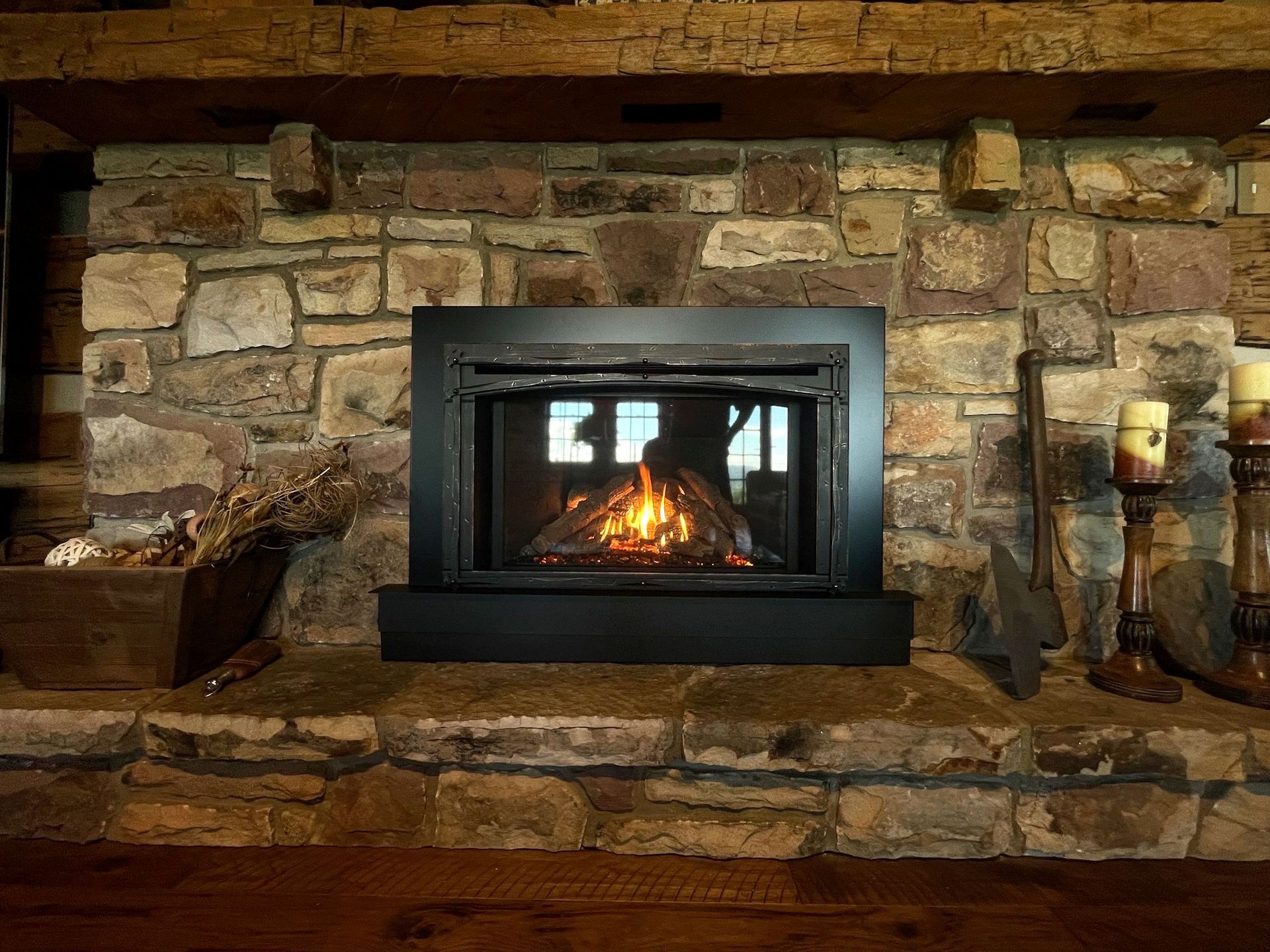 Fireplace with burning flames in a stone-walled setting. Candles and rustic decor surround.