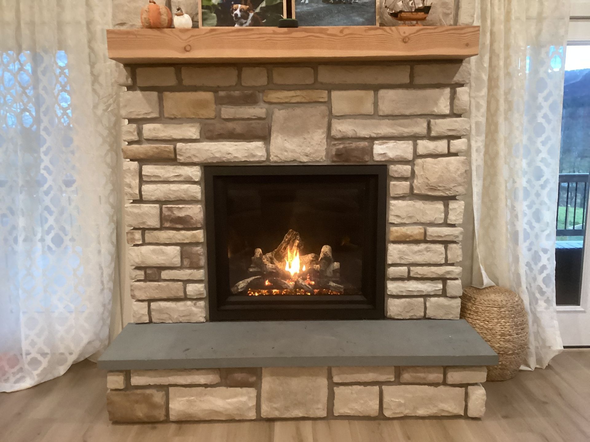 Stone fireplace with a lit fire, wood mantel, and gray hearth.