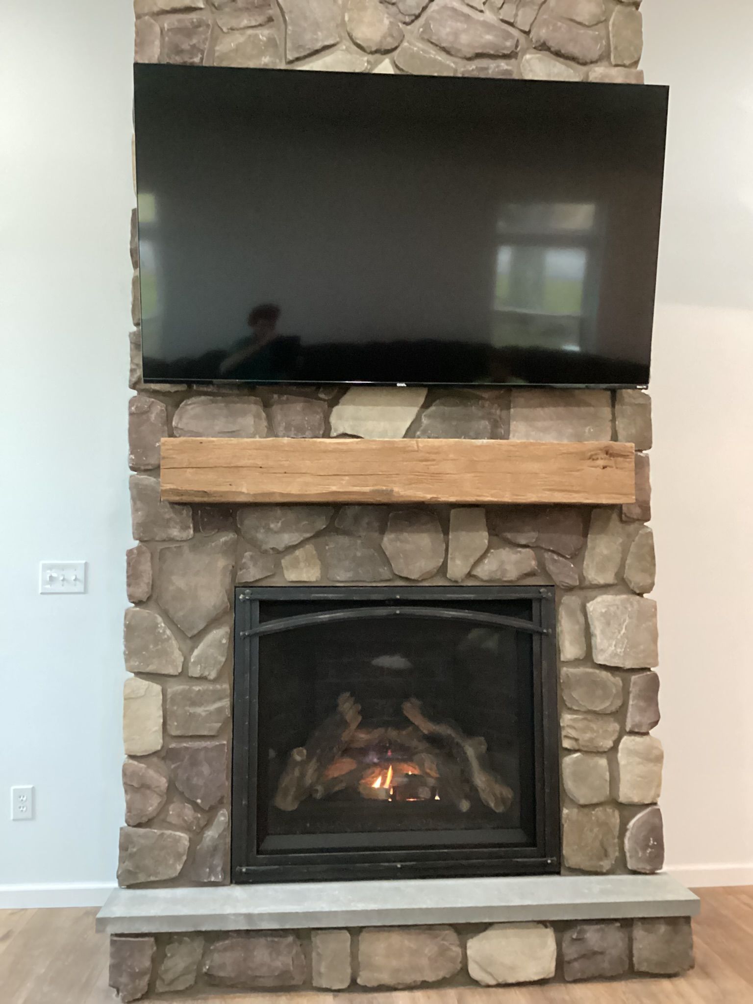 A stone fireplace with a lit fire, wooden mantel, and a mounted television above.