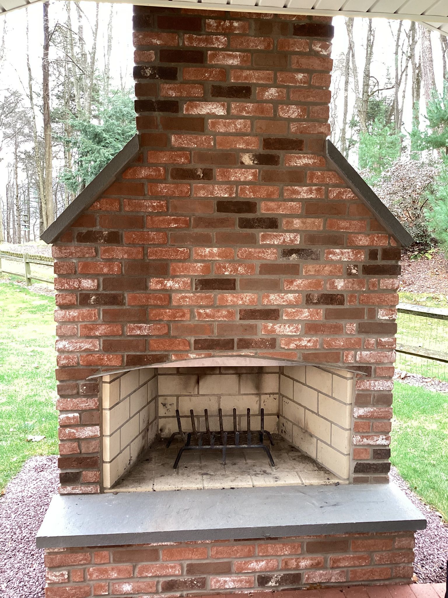 Brick outdoor fireplace on stone base, with grill and chimney.