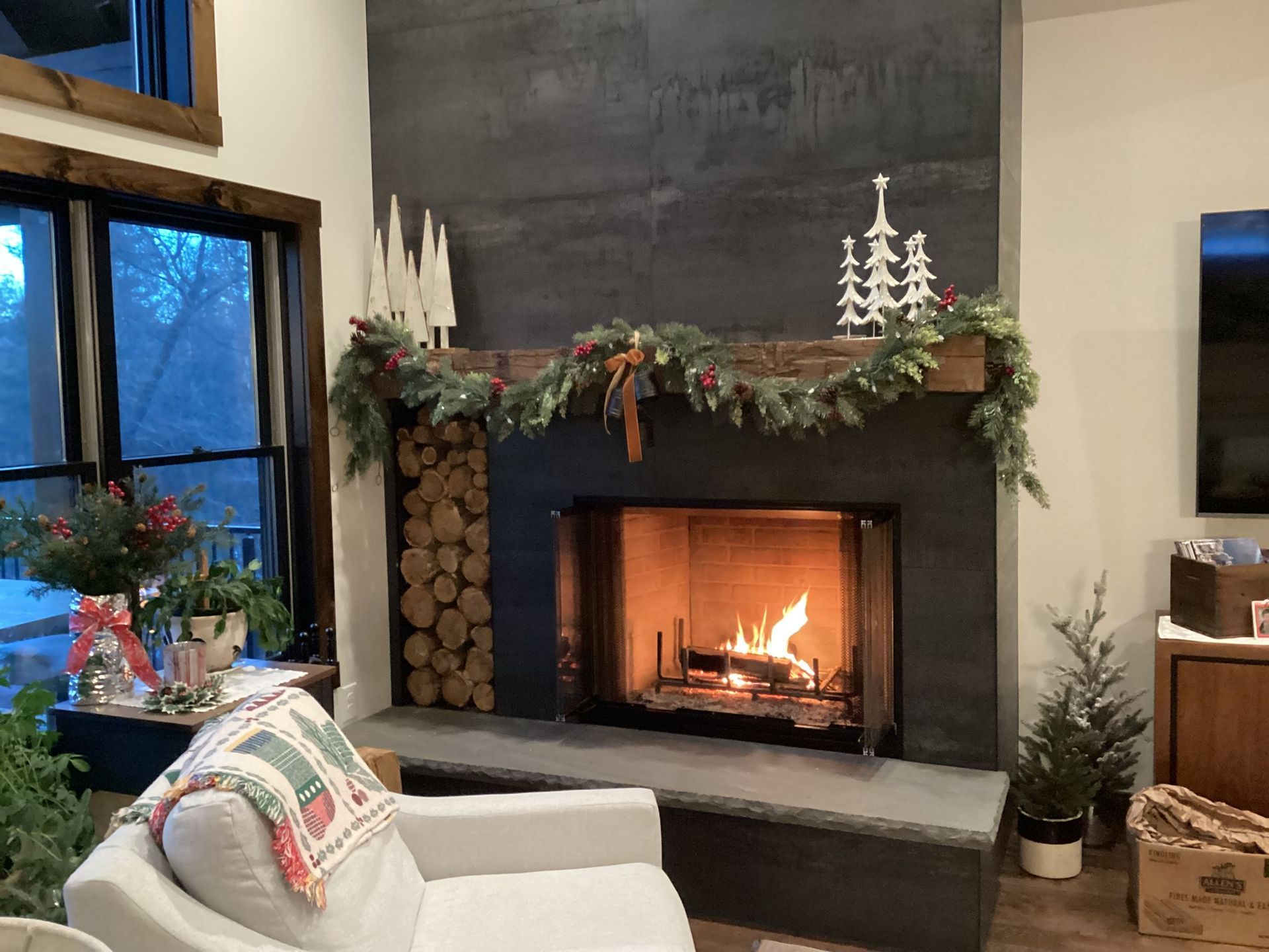 Cozy fireplace with a lit fire, decorated with garland and Christmas ornaments. A white couch sits in front of it.