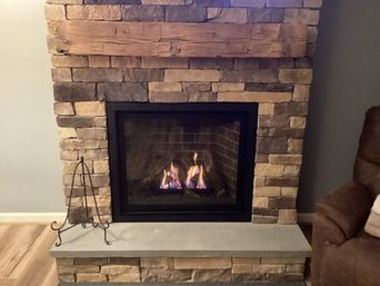 Fireplace with stone surround and wooden mantel, burning gas flames.