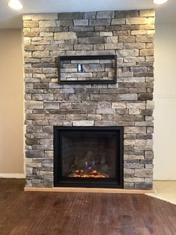 Stone-faced fireplace with a black mantel and a television mount, on a wood floor.