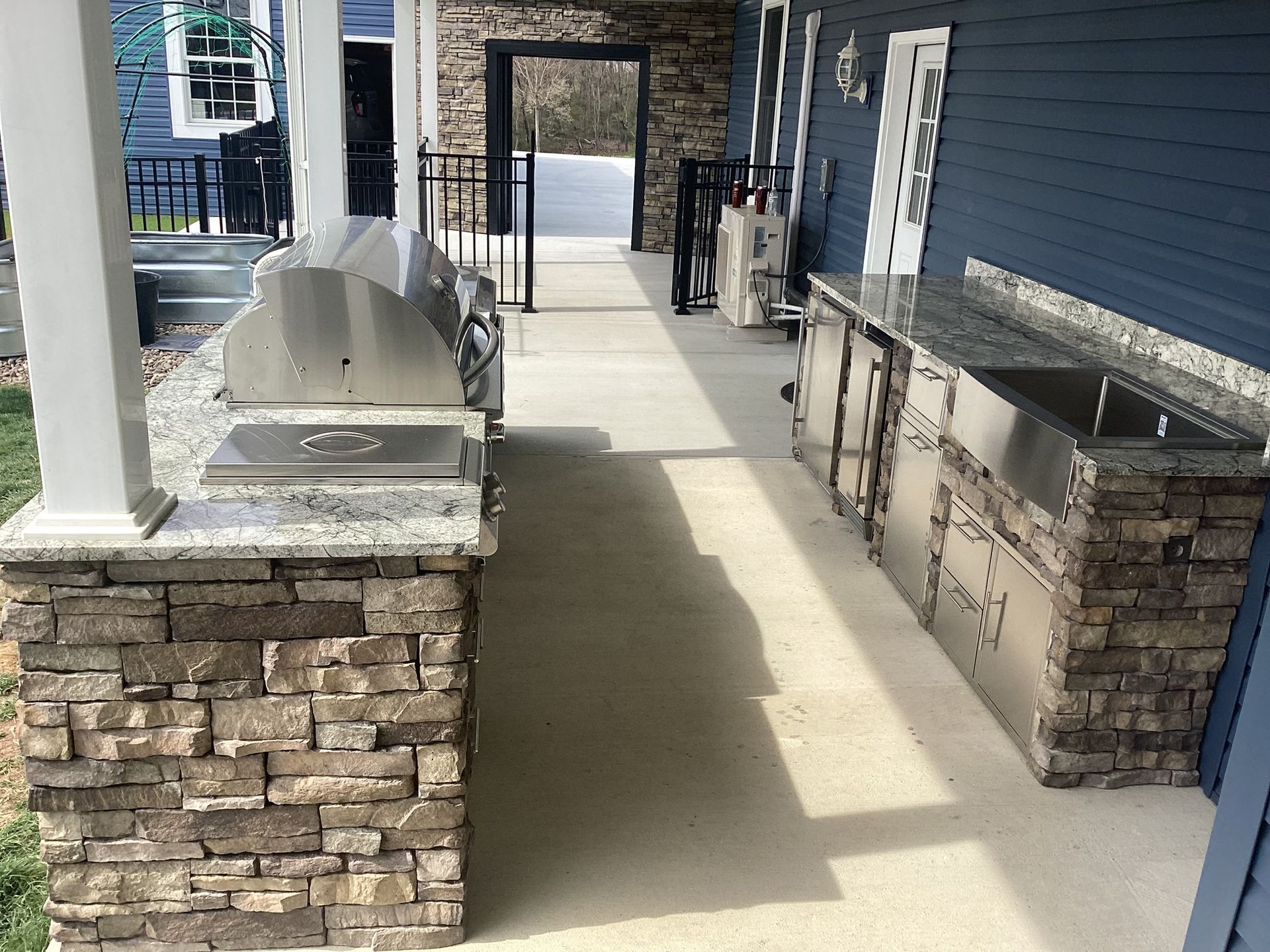 Outdoor kitchen with stainless steel appliances, stone facade, and blue siding.