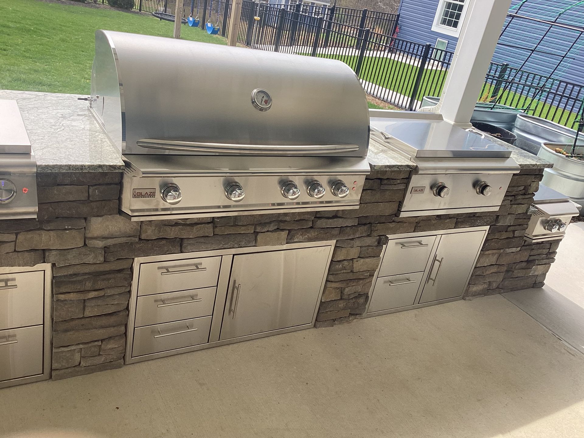 Outdoor kitchen with stainless steel grill, cabinets, and stone facade.